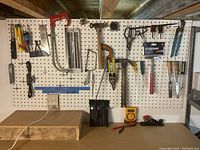 Hand tools hanging on pegboard including saws, hammer, pliers, scissors, and measuring tools.