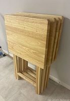 Four wooden TV tables with stands nested together, showing natural wood grain and light finish.