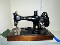 Side view of vintage black Singer sewing machine with gold lettering, mounted on a wooden base.