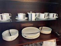 Eight cups and saucers with Parallel stripe pattern displayed on shelf alongside creamer and sugar bowl