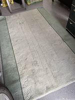 Full view of the wool area rug showing the light beige center and sage green border with embossed leaf design.