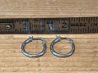 Pair of polished white gold hoop earrings laid out side by side with measuring ruler showing each hoop is about 1-inch diameter.