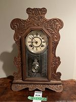 Front view of antique wooden gingerbread mantle clock showing overall shape, carved details, and glass front pendulum area.