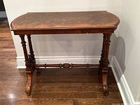 Front view of antique burl walnut console table showing book matched veneer top and carved legs on casters.