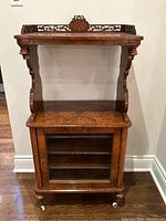 Front view of entire music stand cabinet showing carved gallery, veneered top and glass-door lower cabinet.