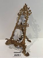 Front angled view of the brass easel showing the overall shape and intricate detailing on the frame.