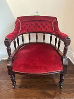 Front view of antique Victorian red velvet buttonback chair showing the carved wood arms, turned spindles, and velvet upholstery.