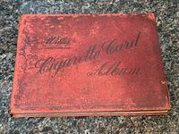 Red hardcover Wills cigarette card album with worn cover and spine, showing age-related wear and fading.