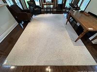 Full view of large light beige Berber style area rug placed on hardwood floor, showing size and color.