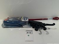 Photo showing a long red metal shoe horn with a bulbous end and sealed Dr Scholl orthotic insoles next to a black cast iron boot jack shaped like an insect.