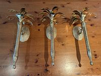 Three brass pineapple-shaped wall candle sconces displayed side by side on a wood surface, showing front view.