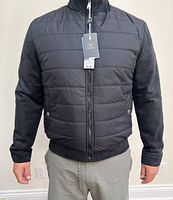 Front view of black men's puffer jacket with suede sleeves, zipper closed, tags attached.