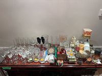 Top-down view showing a large assortment of glassware including clear crystal stemware, various candles in holders, and pewter pieces spread on a wooden table.
