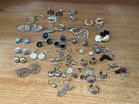 Full lot spread of multiple silver or white metal earrings in pairs and singles on wooden surface.