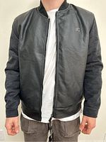 Front view of men's black leather and suede jacket with a zipper and RC logo on the chest, worn by a model.