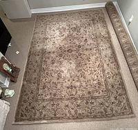 Full view of the Persian style area rug displayed on carpeted floor. Shows pattern and colors including beige, grey, brown and red.