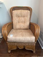 Front view of rattan wicker chair with beige seat and back cushions, showing full chair shape and cushion style.