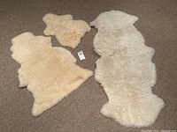 Three sheepskin wool rugs laid on carpet in natural cream to off-white colors, showing full view of rugs.