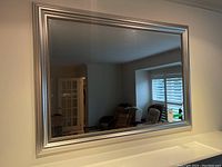 Full view of the large silver framed mirror hung on a wall, showing room reflection.