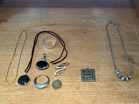 Overview of sterling silver jewelry lot showing pendants, necklaces, earrings, bracelet, and napkin ring on wooden surface.