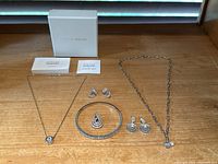 Photo showing the full set of jewelry including necklace, bracelet, earrings, pendant, and original packaging and care cards
