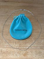 Sterling silver chain necklace laid out around Tiffany & Co. turquoise drawstring pouch on wooden surface