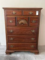 Front view of vintage solid wood highboy dresser showing six drawers and brass shell detail on middle drawer