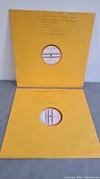 Two 16-inch records housed in yellow sleeves with handwritten notes.