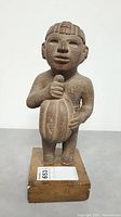 Front view of the vintage Aztec man stone figure holding a cacao pod, mounted on a wooden base.