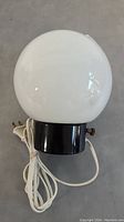 Front view of white glass globe lamp on black base with cord coiled next to it.