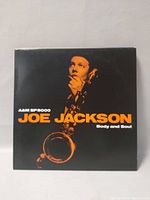 Front cover of Joe Jackson Body and Soul LP showing Joe Jackson with a saxophone against a black background with orange text.