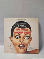 Front cover of The Rocky Horror Show Original Cast soundtrack album showing illustrated face of a shocked woman with earrings and bold red title text.