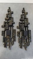 Pair of two Mid-Century Modern wall-mounted candlestick holders with geometric patterned rectangles and squares in bronze and black finish, arranged side by side on a flat surface.