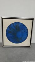 Full view of framed blue glass plate artwork showing the circular plate centered in a white mat within a black frame against a neutral background.