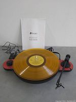 Turntable assembled on red plinth with yellow LP, manual, power adapter and cables visible
