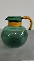 Front view of vintage green glass water jug with yellow wrapped handle, showing bulbous body and pouring spout.