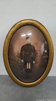 Front view of oval framed vintage military soldier photo showing wear on gold-colored frame.