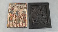 Stoneware Egyptian themed wall plaque with colorful figures and hieroglyphics alongside the carved wooden panel.