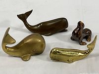 Four sea animal figurines: largest brass whale, medium brass whale, small brass whale, copper-finished sea lion.