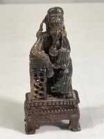 Front view of carved soapstone figurine of a man seated on pedestal showing detailed robe and headpiece