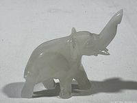 Front and side view of a small carved elephant figurine made of a white translucent stone with a raised trunk.