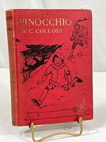 Front cover of vintage Pinocchio book showing red cloth with gold text and black illustrations.