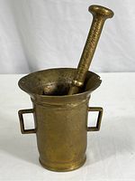 Vintage solid brass mortar with two handles and pestle inside, showing overall shape and design