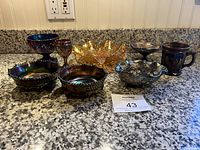 Full view of all eight carnival glass pieces arranged on a countertop showing variety of styles and colors.