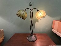 Front view of the antique lily pad table lamp on a wooden surface showing both shades, one lit and one unlit.