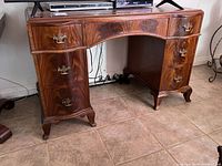 Front view of the antique mahogany writing desk showing curved middle drawer and side drawers with brass handles, and bracket feet.