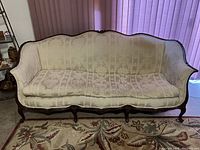 Full front view of antique style Rococo sofa with light silk upholstery and carved dark wooden frame.