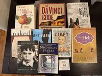 Nine assorted books including four hardcovers and five paperbacks placed on a dark surface