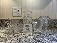 Five early American pressed glass pieces displayed on granite countertop including small pitchers and vessels with intricate patterns.