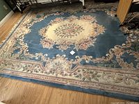 Full view of large Aubusson rug on wooden floor showing floral and ornamental central patterns with a beige and pink border and fringes.